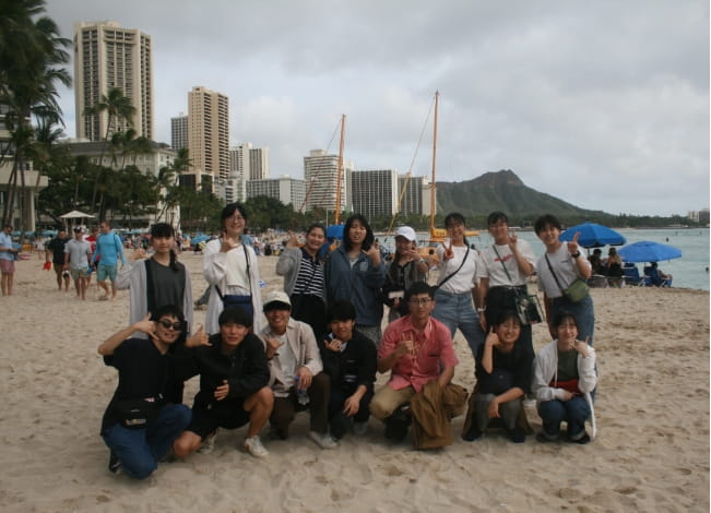 海辺で学生たちがポーズをとりながら集合写真を撮影している。